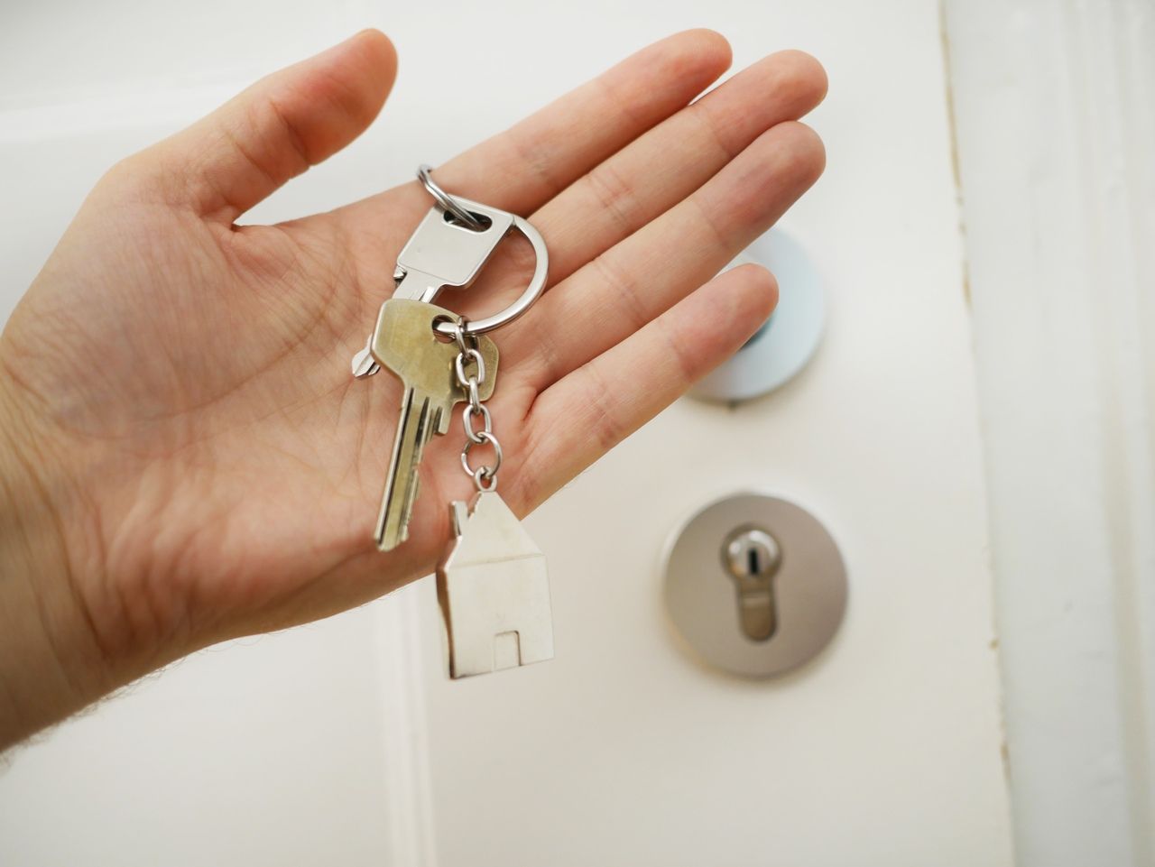 Hand holding house keys next to a property door after a real estate close