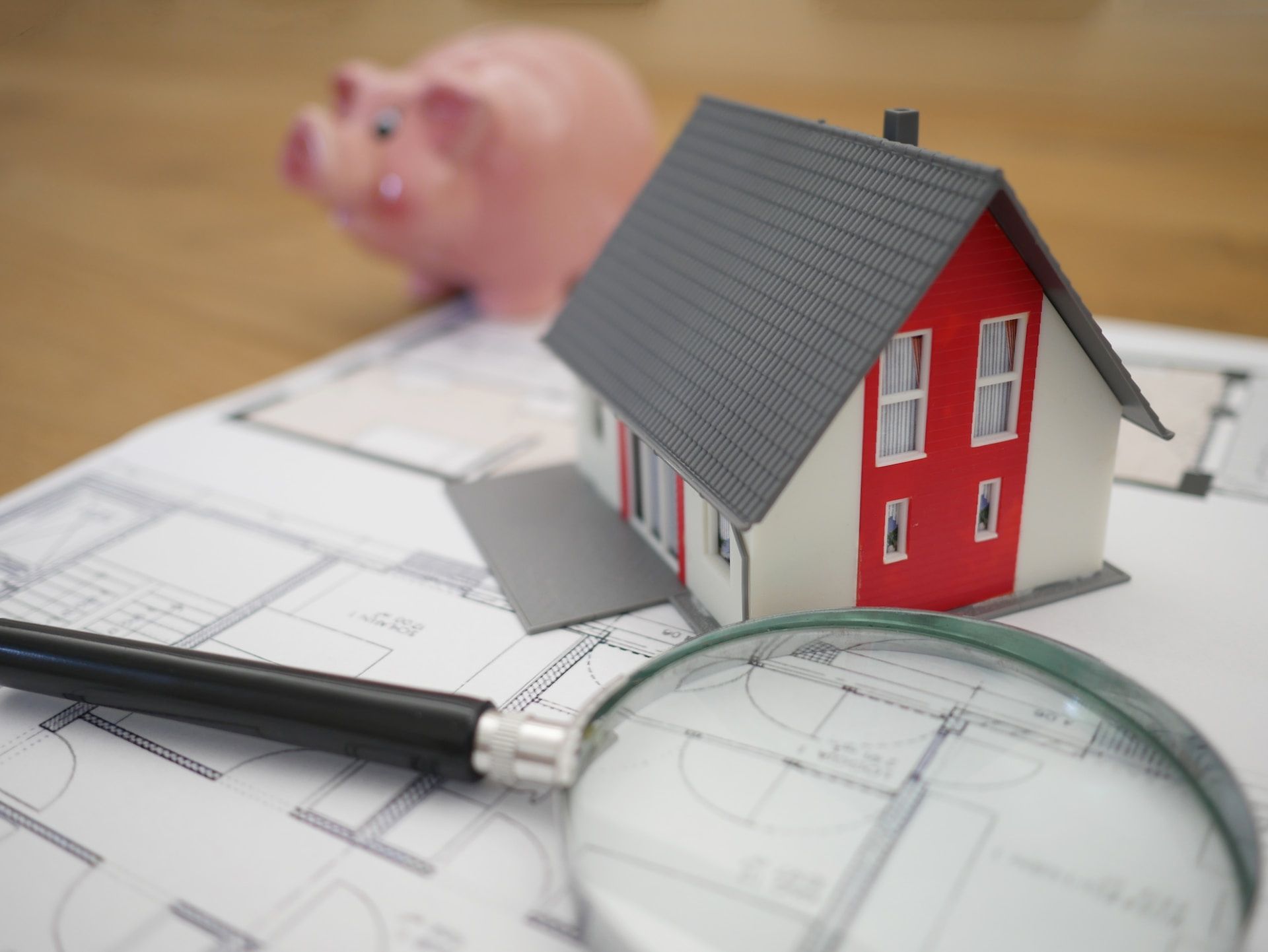 Wooden model house next to a magnifying glass representing real estate searches
