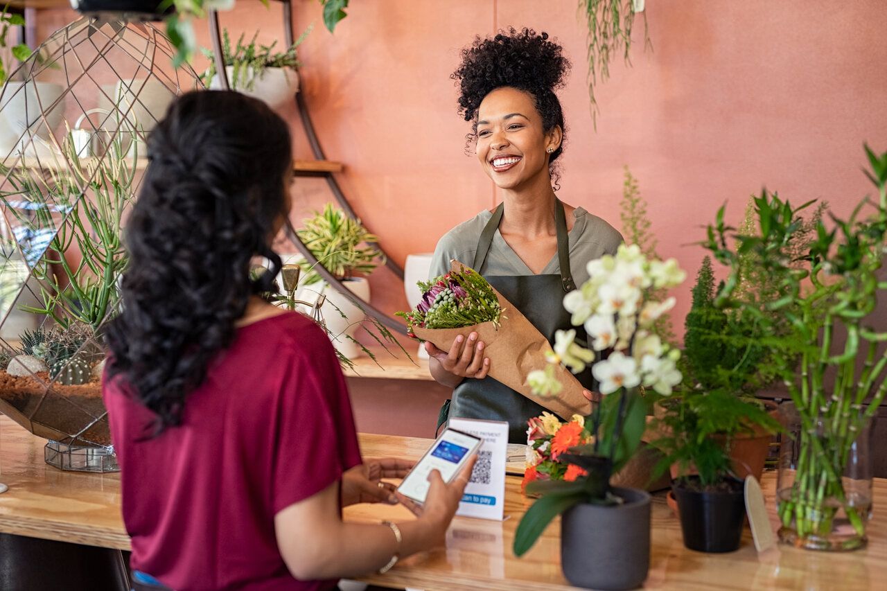 Florist handing a bouquet to a customer next to a counter receipt with a QR code