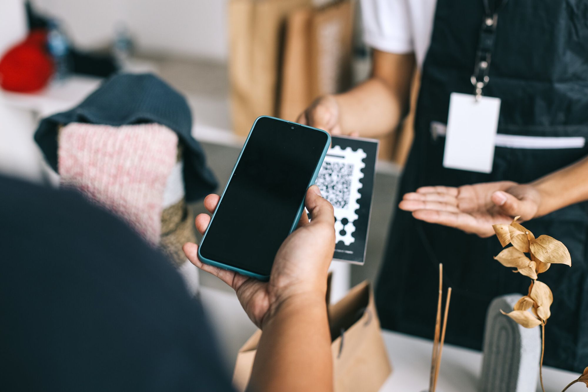 Hand holding an Android smartphone scanning a QR code printed on a retail counter surface