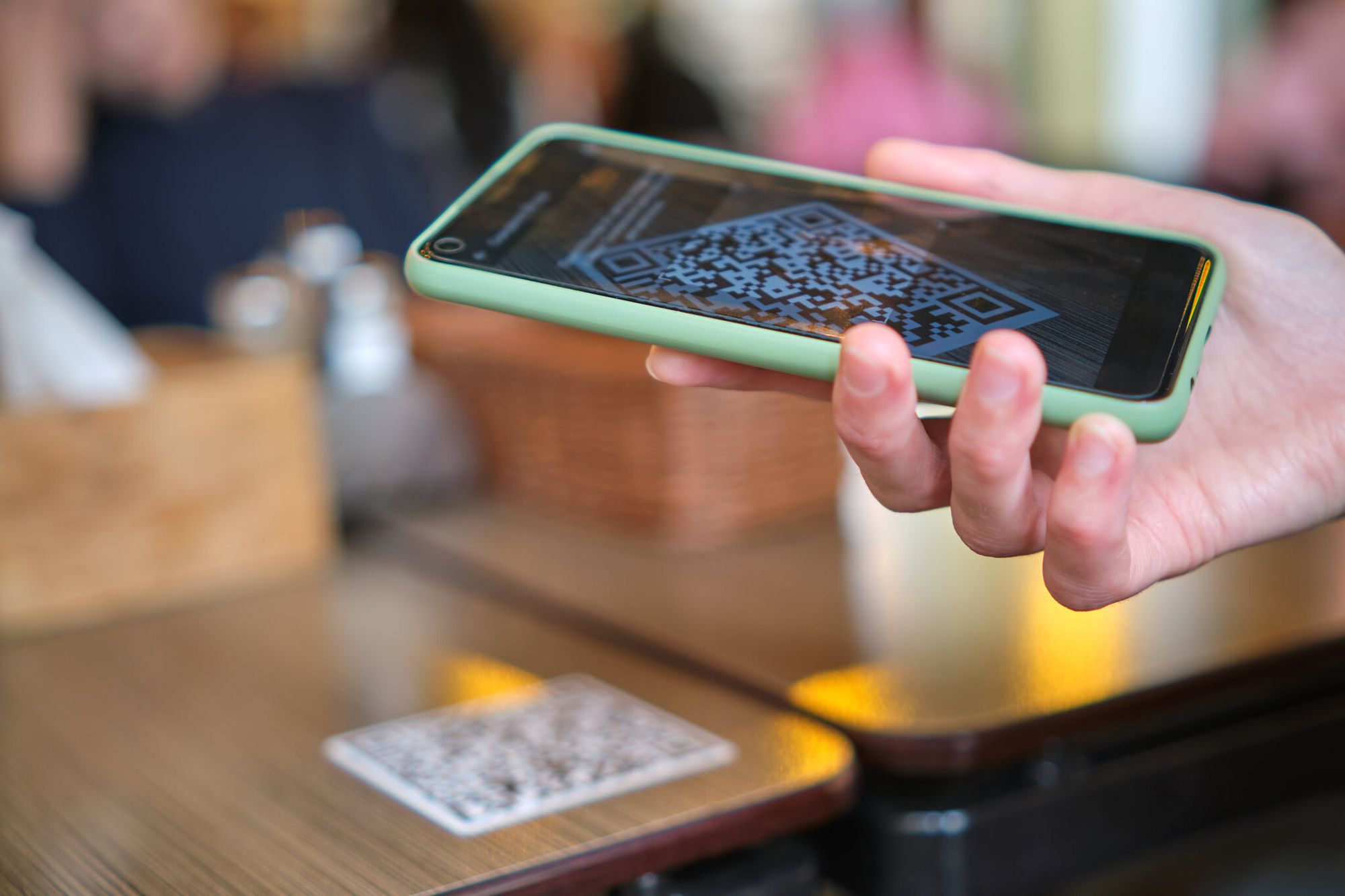 Closeup of a hand holding a smartphone scanning a QR code on a wooden cafe table for app install