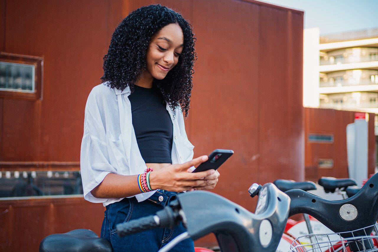 A young woman on a bicycle smiling as she scans a QR code with her phone
