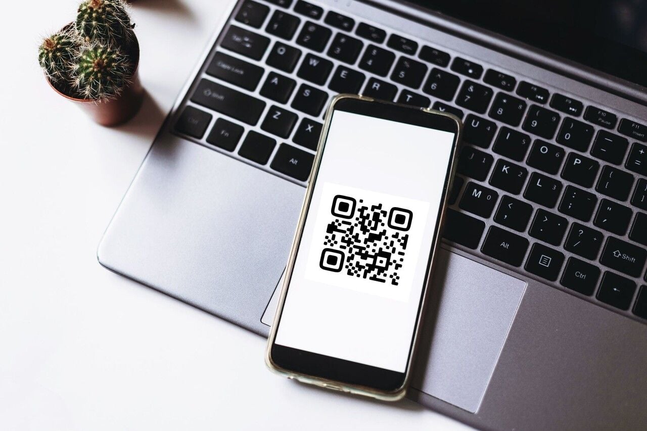 A phone scanning a QR code displayed on a computer screen, illustrating cross-device clickable QR code use